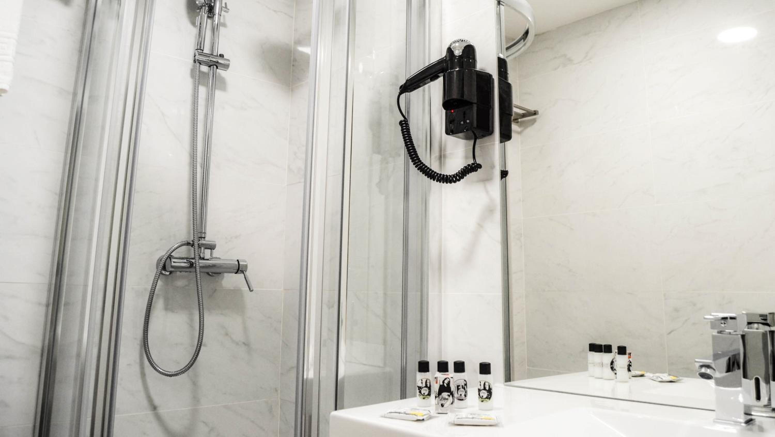 Une salle de bain moderne dotée d’une douche à parois de verre, d’un pommeau de douche à main et d’un miroir avec des articles de toilette.
