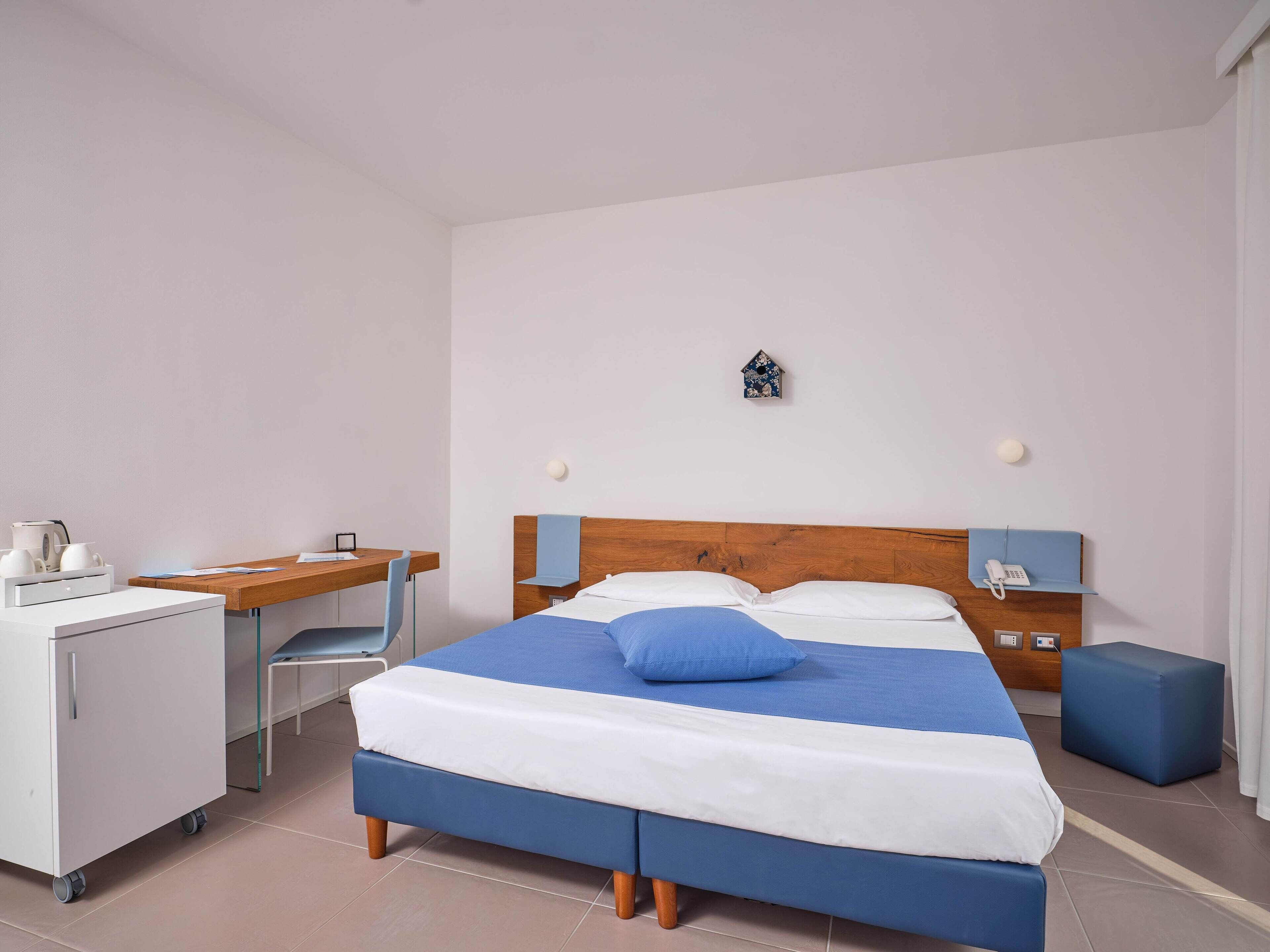 A hotel room with a bed, a desk, a chair, a small table, and a cabinet.