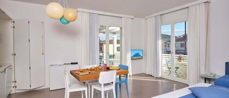 A modern hotel room with a balcony, a dining area, and a bed with blue bedding.