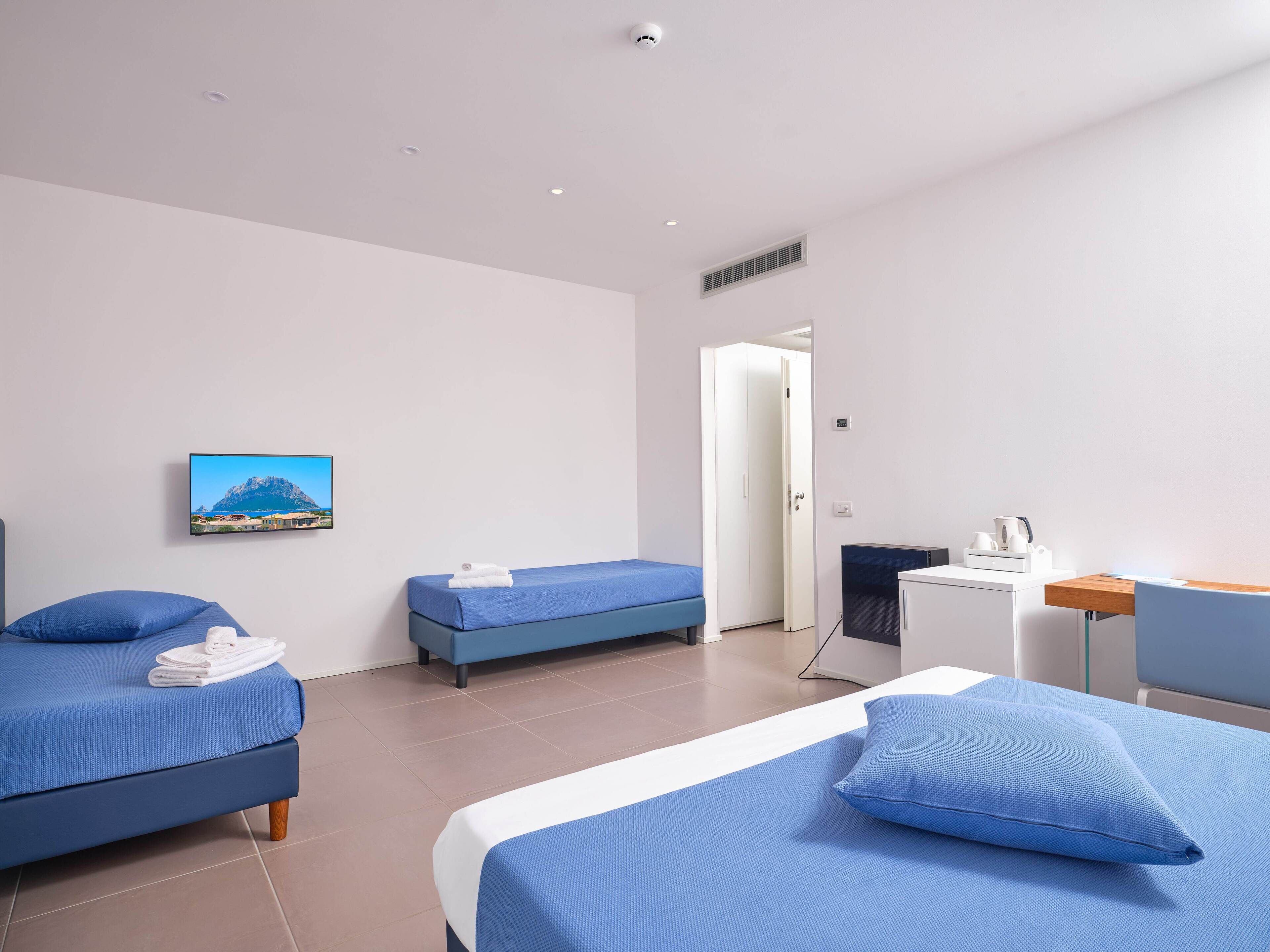 A hotel room with two beds, a desk, a chair, a TV, and a door.