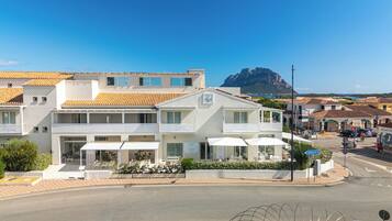 Un hôtel moderne doté d’une terrasse, avec une montagne en toile de fond et un ciel bleu dégagé.