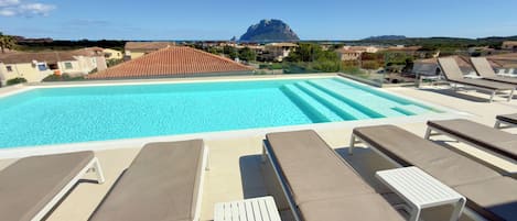 Piscina con sillones de descanso y vista a la montaña.