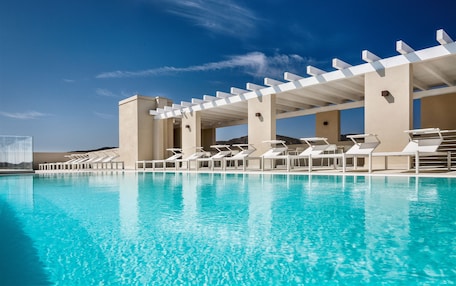 A clear blue pool with white sun loungers and a pergola structure.