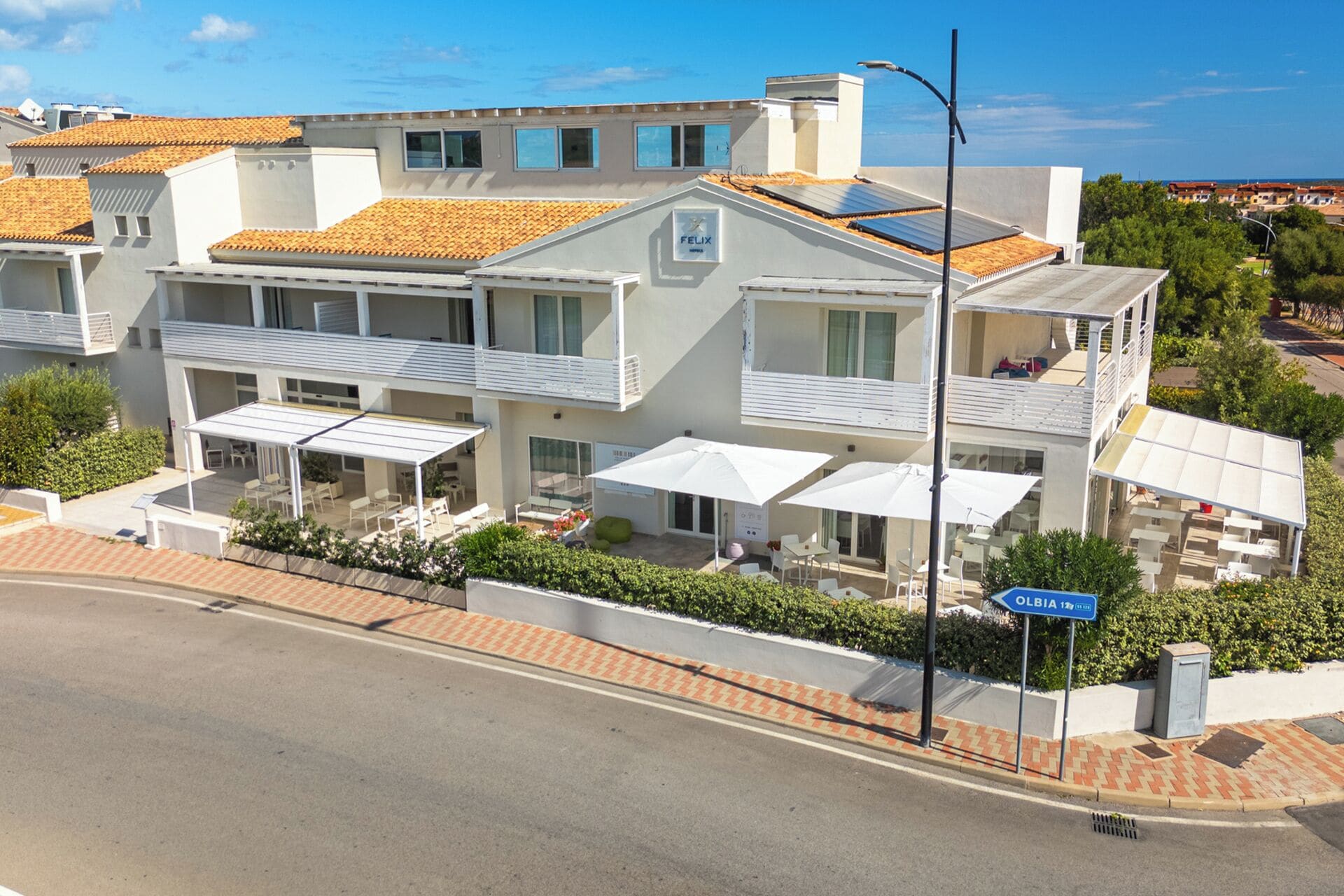 A modern hotel with multiple balconies, outdoor seating, and a clear view of the sea.