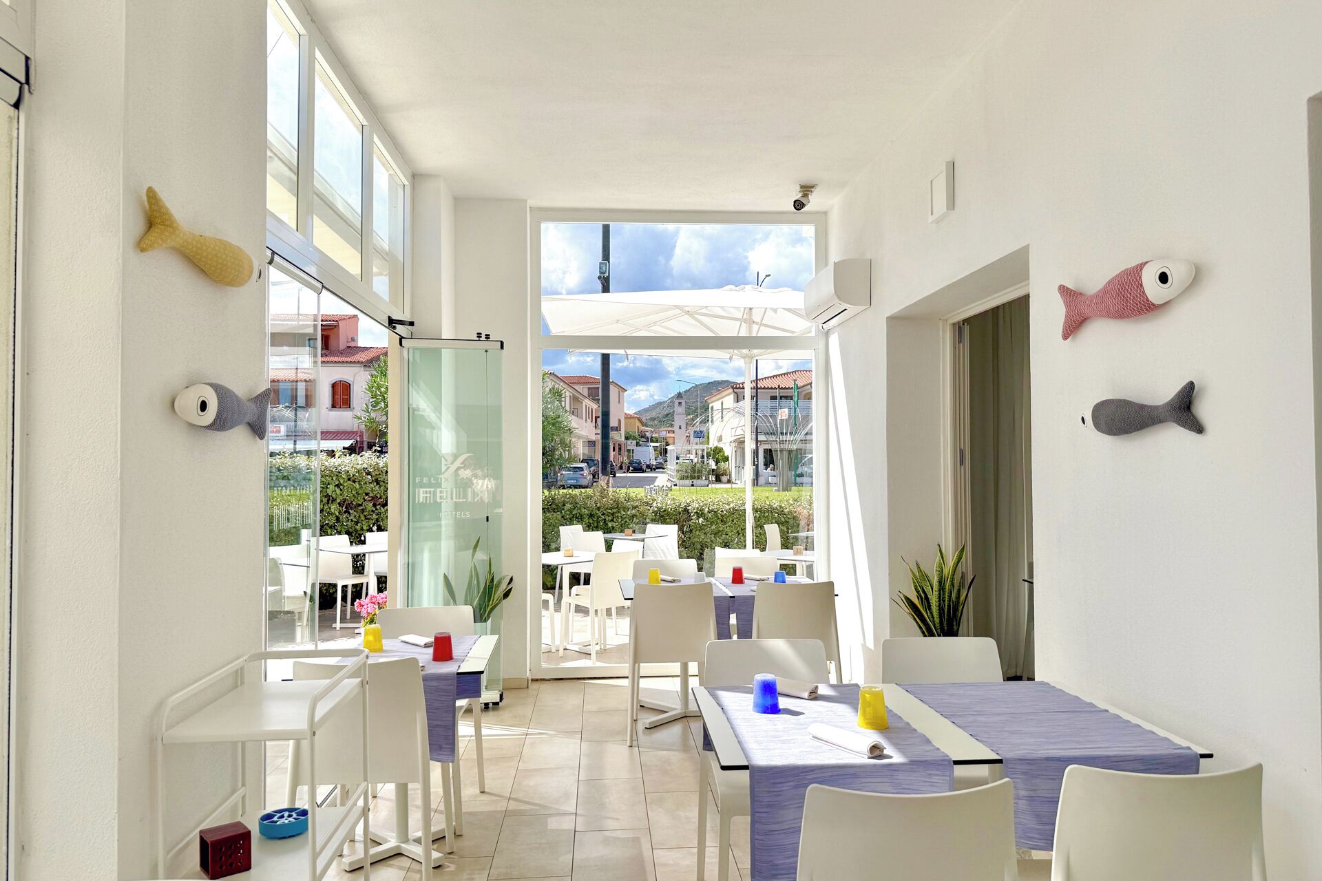 A hotel room with a view of the street, a balcony with outdoor seating, and decorative fish on the walls.