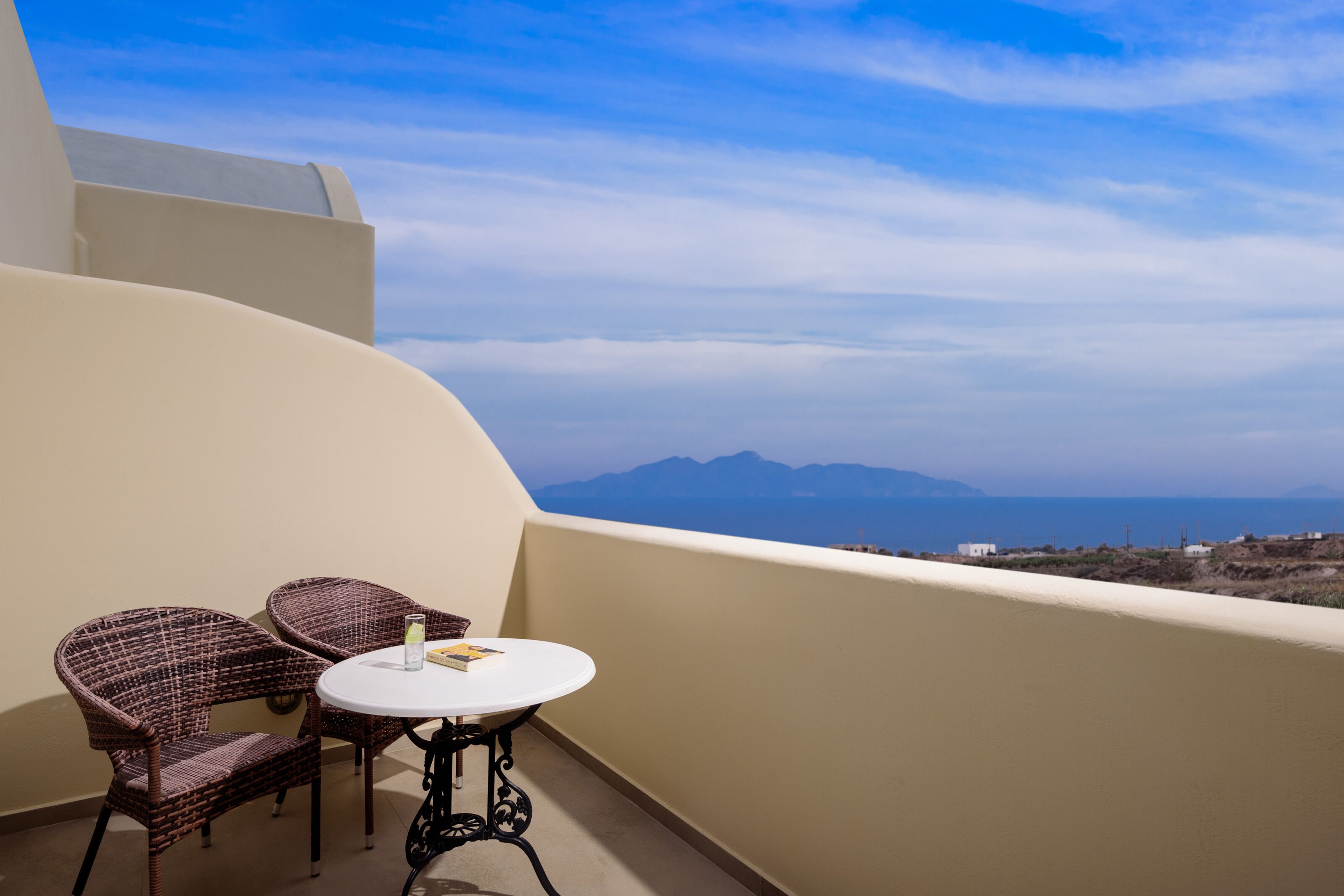 Un balcon avec une table ronde et deux chaises en osier, donnant sur un paysage montagneux.