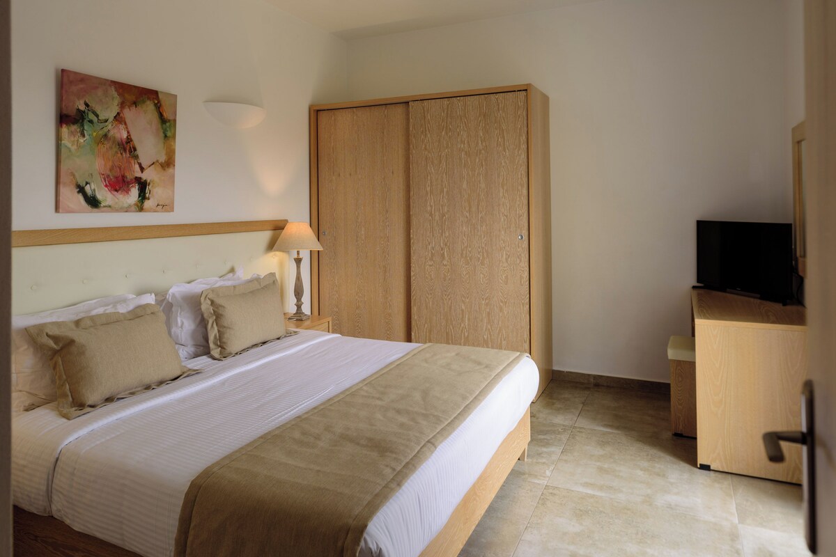 A neatly made bed with a wooden headboard, a bedside lamp, and a painting on the wall.