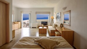 Una habitación de hotel moderna con una cama grande, un sofá, un escritorio y un televisor. Cuenta con un balcón con vistas al mar.