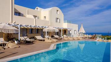Relax by the pool surrounded by lounge chairs and umbrellas, with the ocean view in the background.