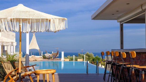 Zona junto a la piscina con vista al océano, sillones de madera para tomar el sol, una palapa y una zona de bar.