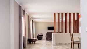 A spacious living area with a neutral color scheme, a flat-screen TV mounted on the wall, and a wooden partition.