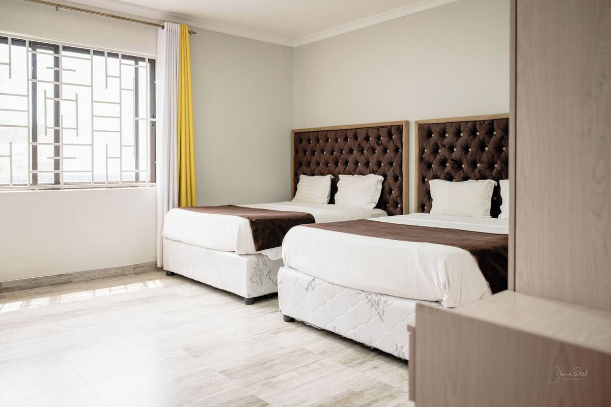 A hotel room with two beds, a window with a geometric pattern, and a light-colored floor.