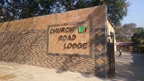 A sign for Church Road Lodge with a stone wall and a green signboard.
