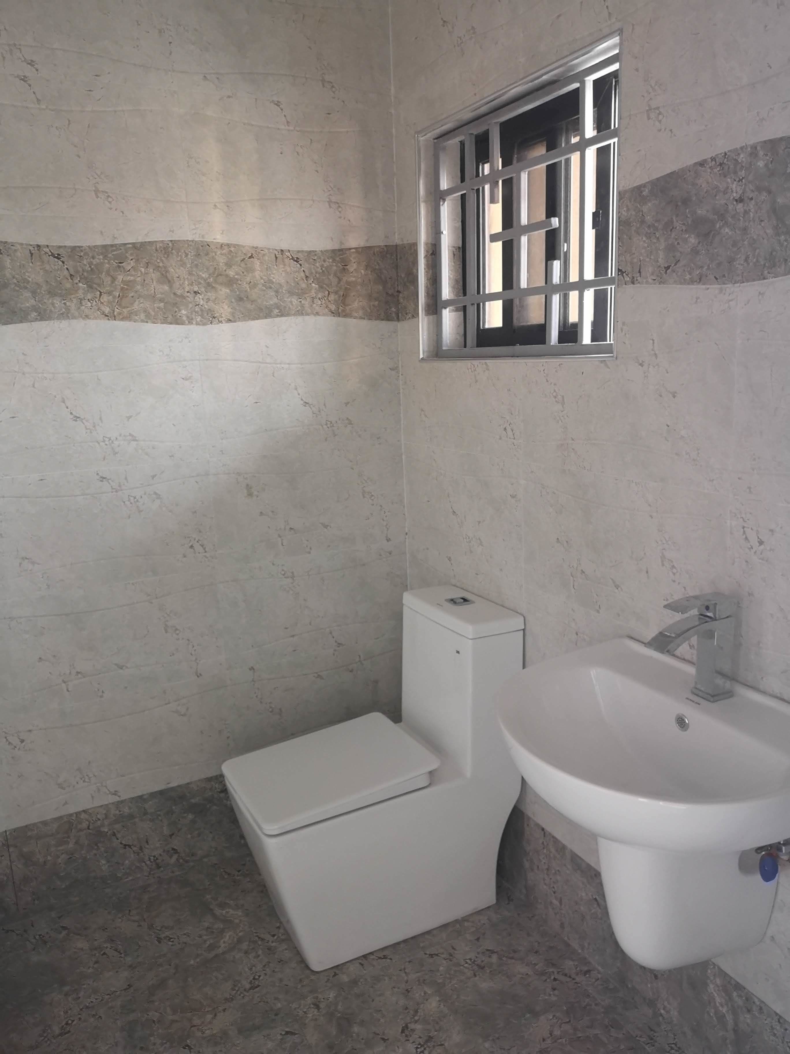 A bathroom with a toilet, sink, and a window with bars.