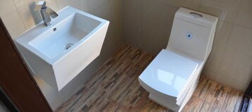 Un baño con lavamanos y retrete blancos, suelo de madera y paredes de azulejos.