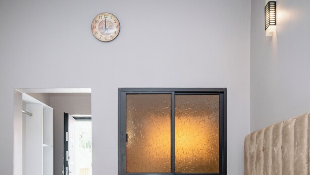 A modern bedroom with a large bed, a sofa, and a wall-mounted clock.