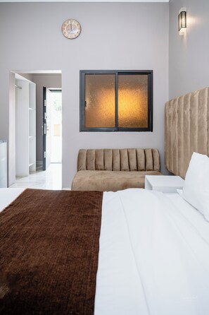A modern bedroom with a large bed, a sofa, and a wall-mounted clock. - Ten Twelve Lodge Limited (Lusaka)