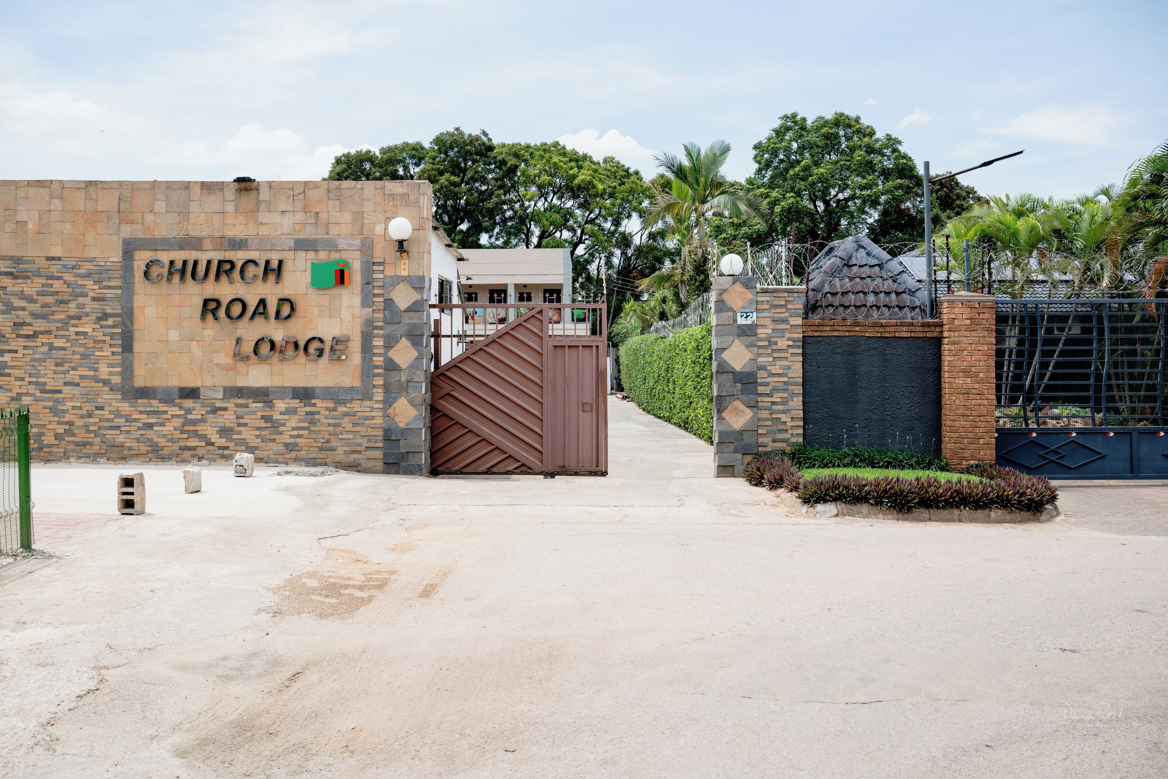A gated entrance to a property named Church Road Lodge, featuring a stone wall with a sign, a gated driveway, and a building with a balcony.