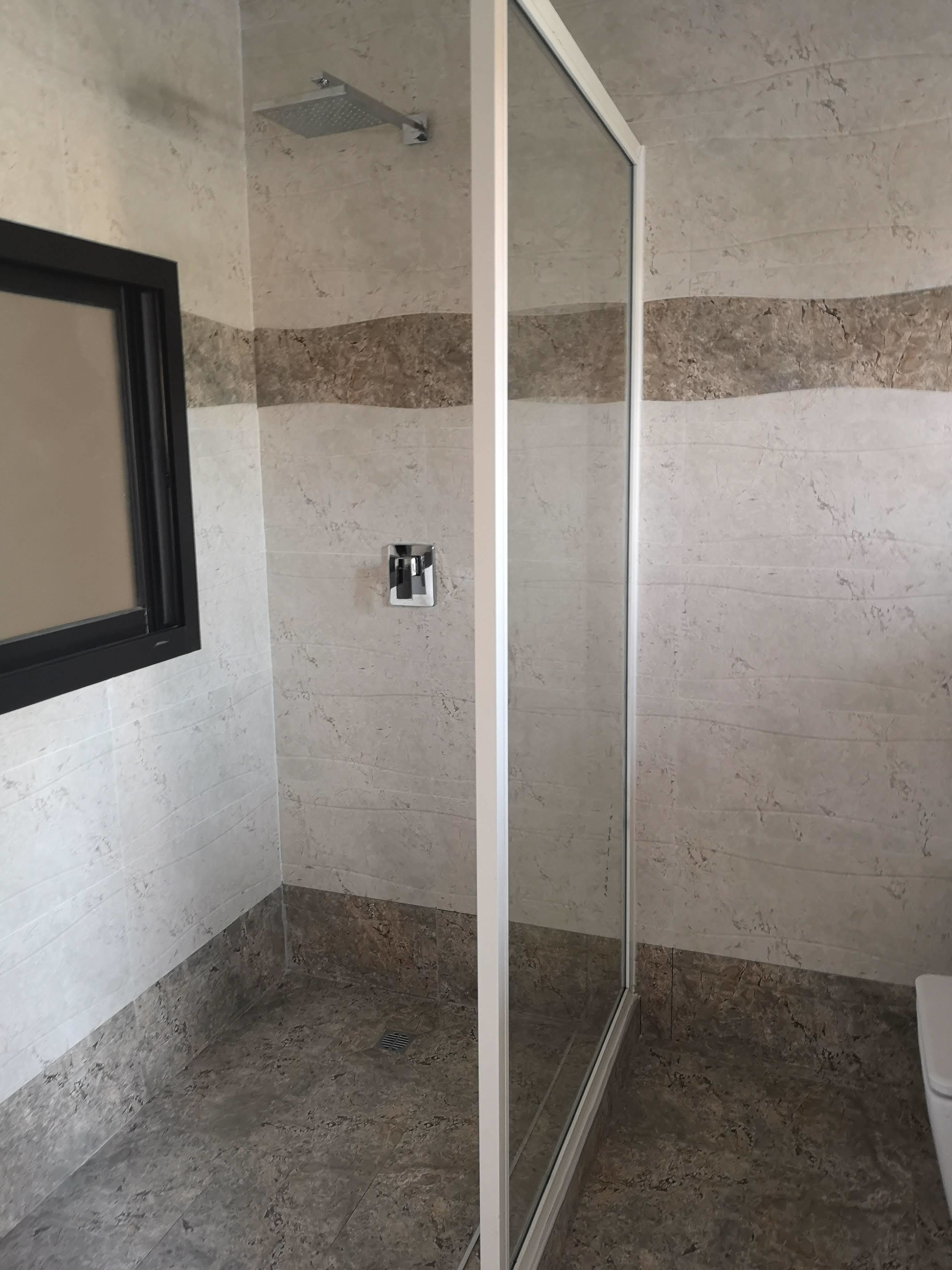 A bathroom with a glass shower enclosure, a toilet, and a sink.