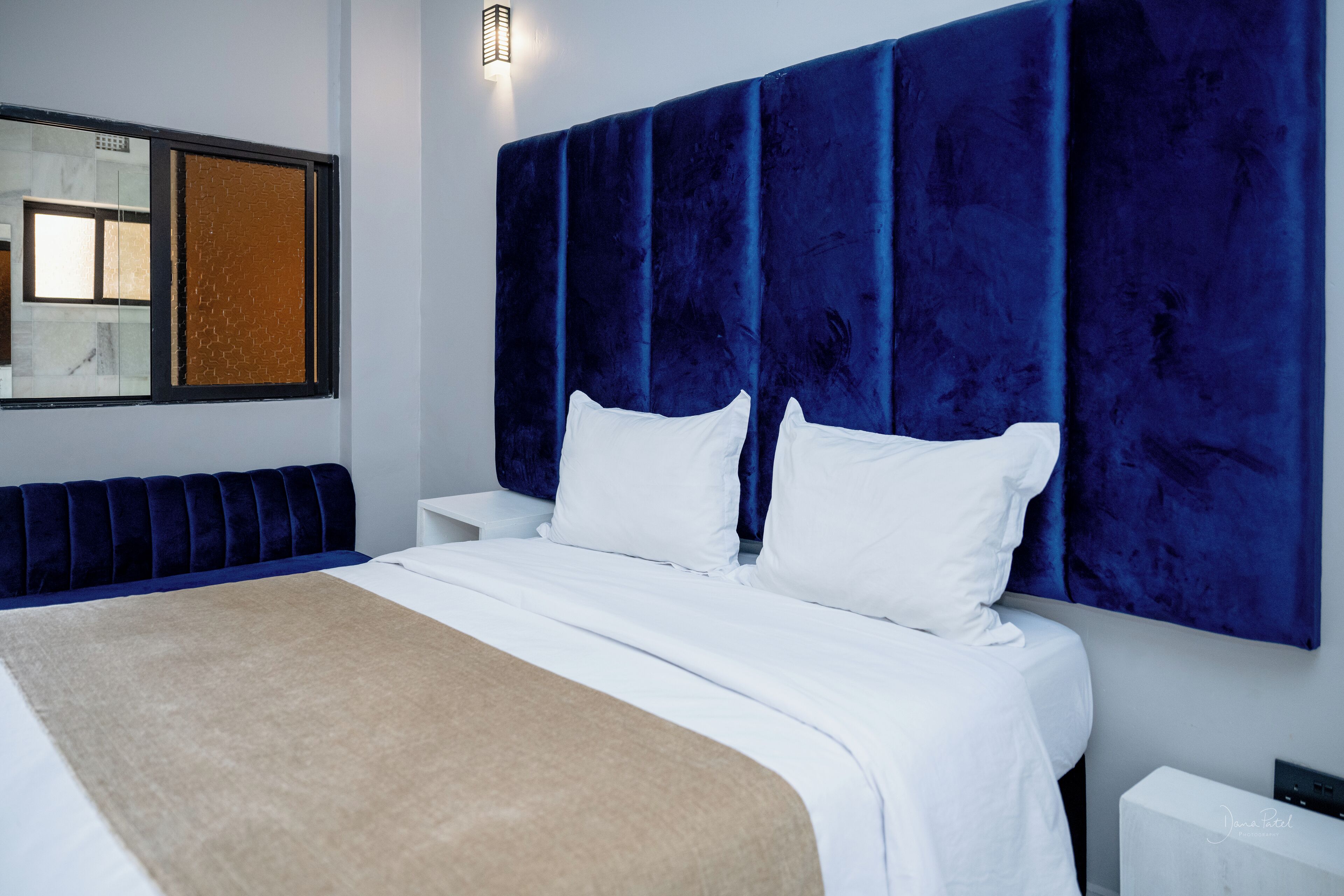 Een moderne hotelkamer met een groot bed, een blauw hoofdbord, witte beddengoed en een bank langs de muur.