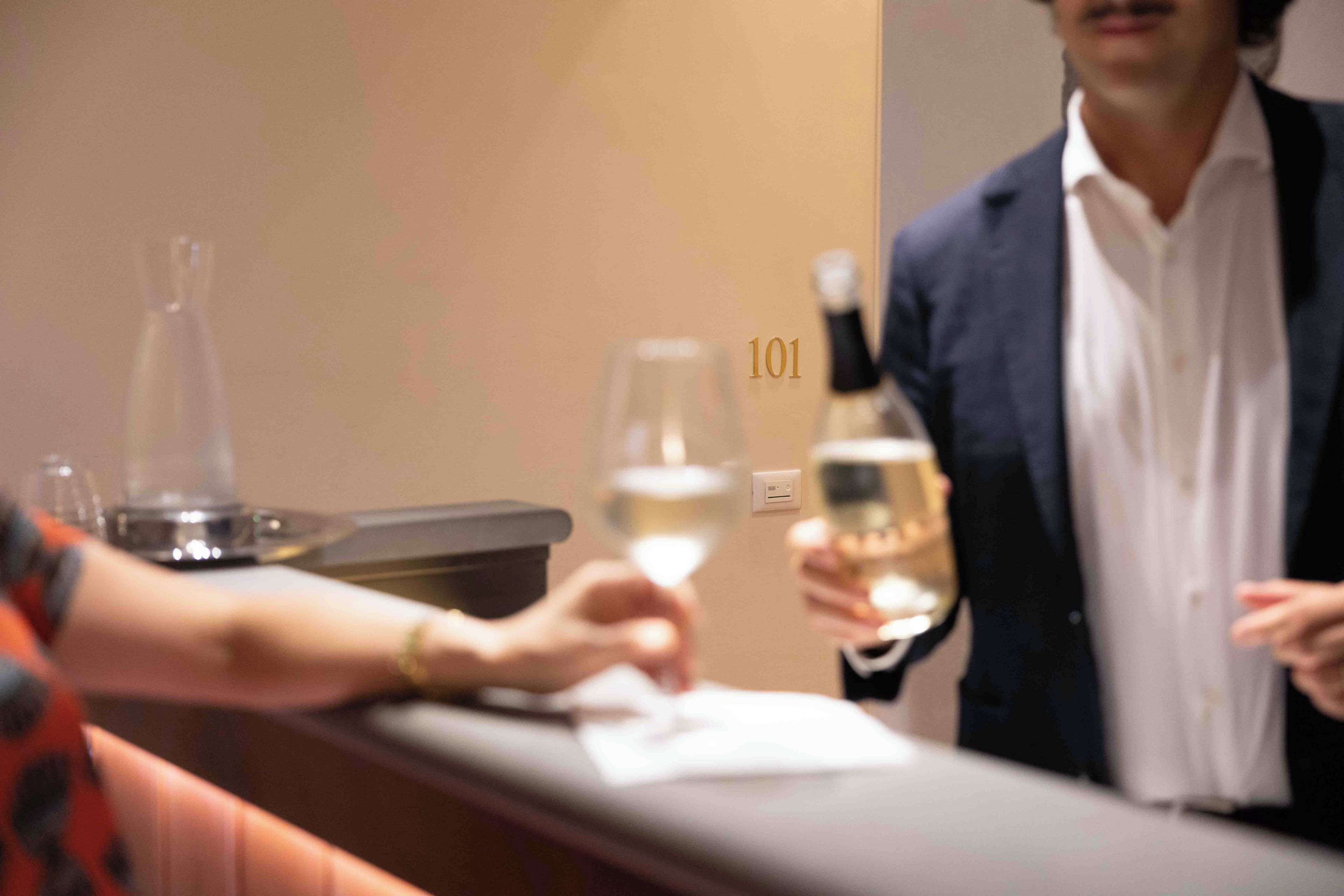 A hotel reception area with a counter, a wine bottle, and a glass of wine.