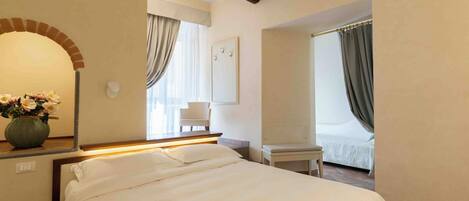 A hotel room with a bed, a chair, a small table, a mirror, and a window with curtains.