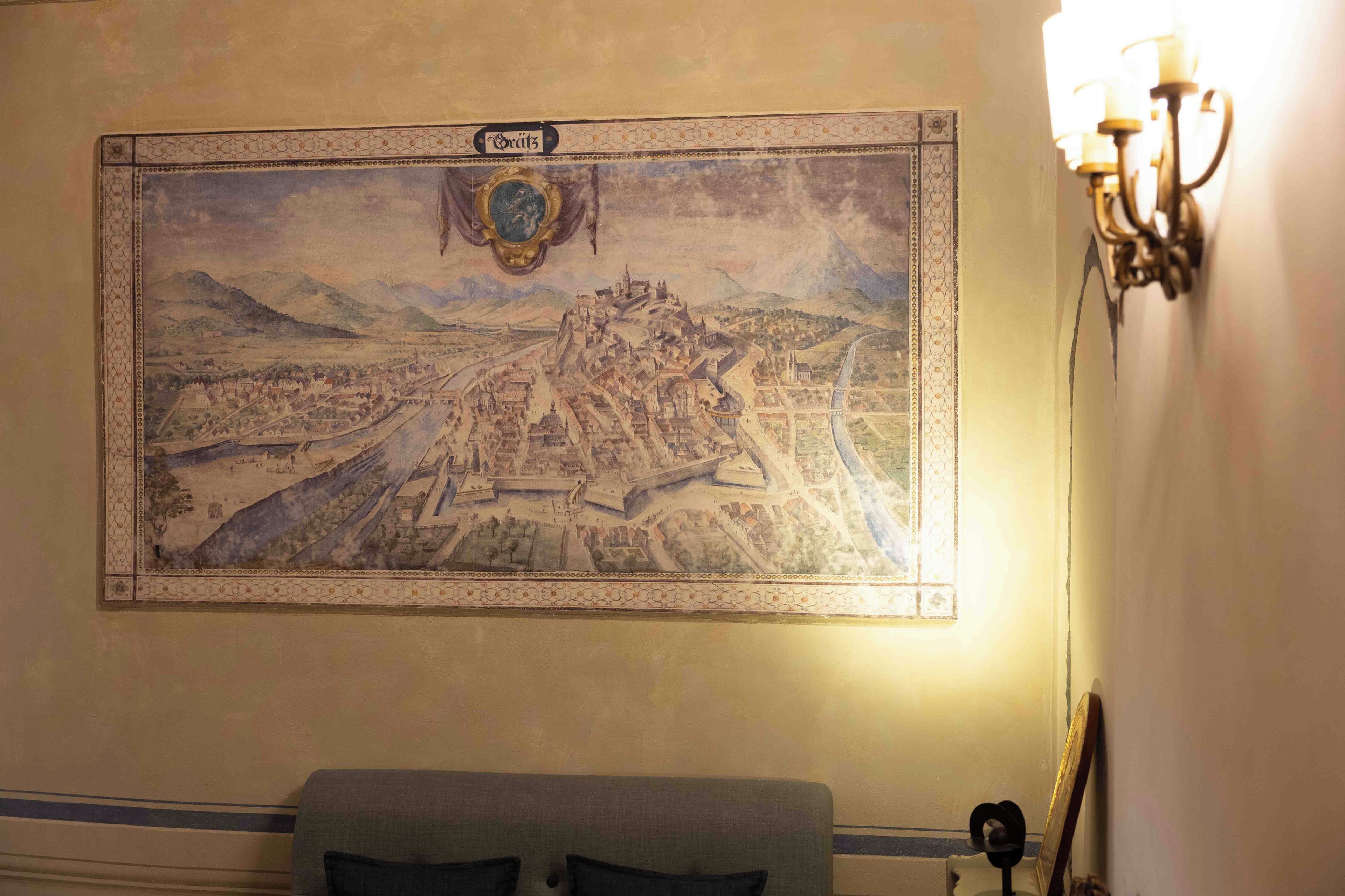 Un mapa colgado en la pared de una ciudad con un castillo destacado, un borde decorativo y una araña.