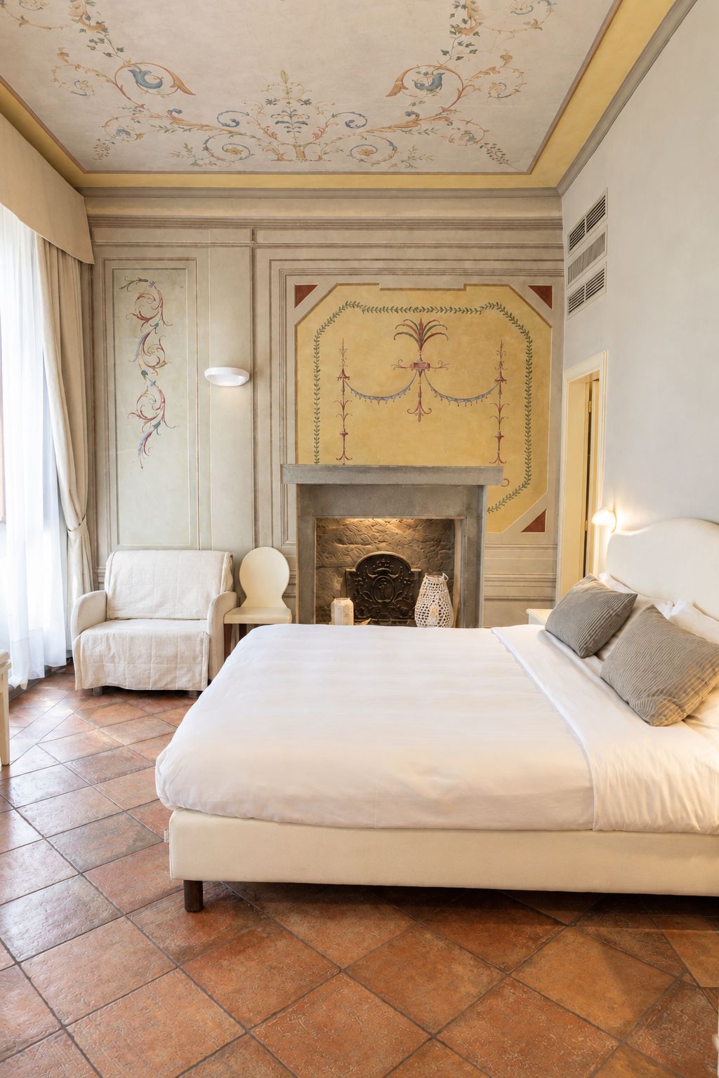 A hotel room with a large bed, a fireplace, a chair, and a decorative ceiling.