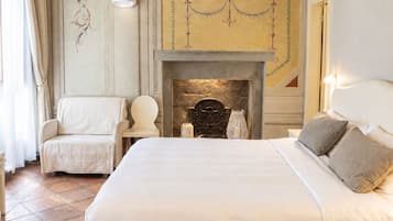 A hotel room with a large bed, a fireplace, a chair, and a decorative ceiling.