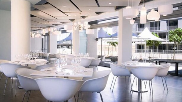 A modern dining area with white tables and chairs, large windows, and hanging pendant lights. - 214 Harbour Bridge (Cape Town)