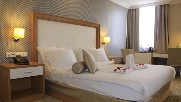 Ein Hotelzimmer mit einem großen Bett, einem Nachttisch mit Telefon, zwei Wandlampen und einem Fenster mit Vorhängen.