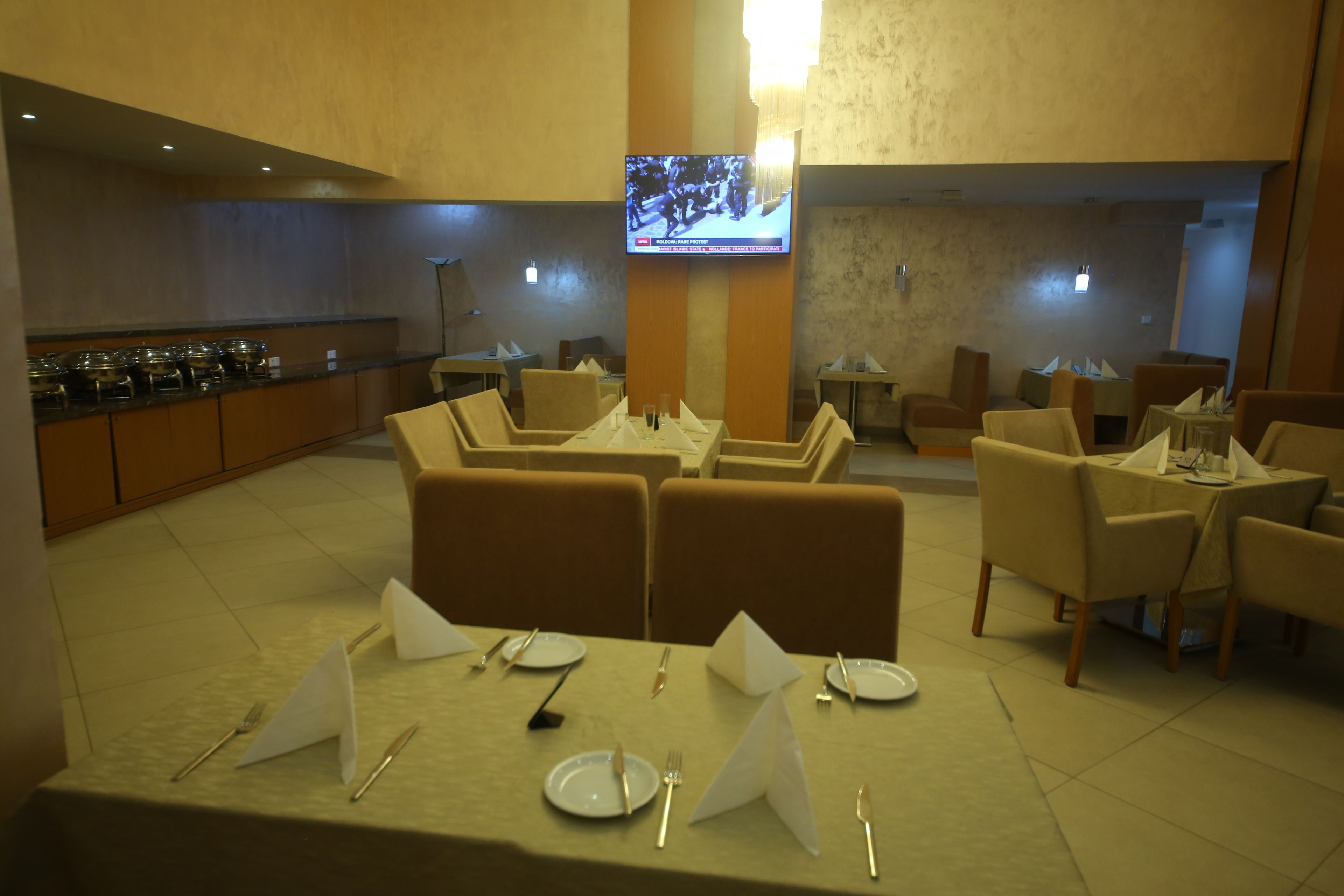 A dining area with tables set for four, a buffet line, and a television mounted on the wall.