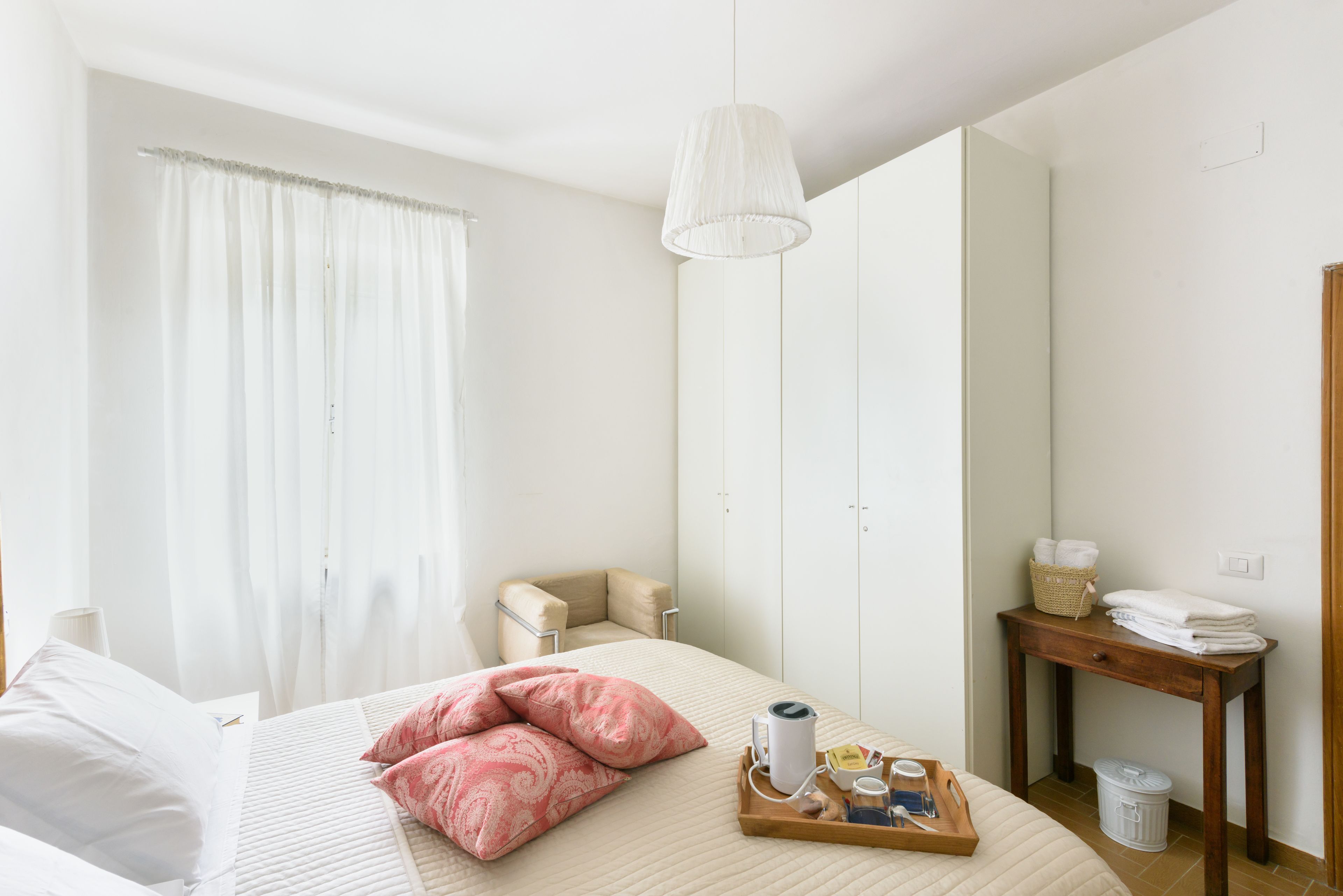 Ein Hotelzimmer mit einem Bett, einem Nachttisch mit Handtüchern, einem kleinen Stuhl, einer Pendelleuchte und einem Fenster mit Vorhängen.