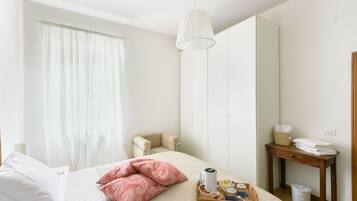 Ein Hotelzimmer mit einem Bett, einem Nachttisch mit Handtüchern, einem kleinen Stuhl, einer Pendelleuchte und einem Fenster mit Vorhängen.