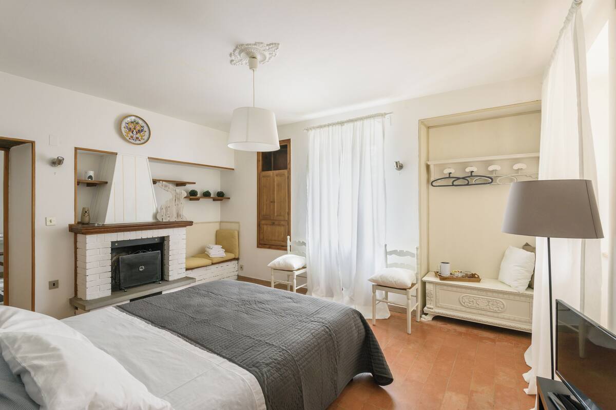 Ein Schlafzimmer mit Bett, Kamin, Spiegel, Kleiderschrank, Stuhl und Fernseher.