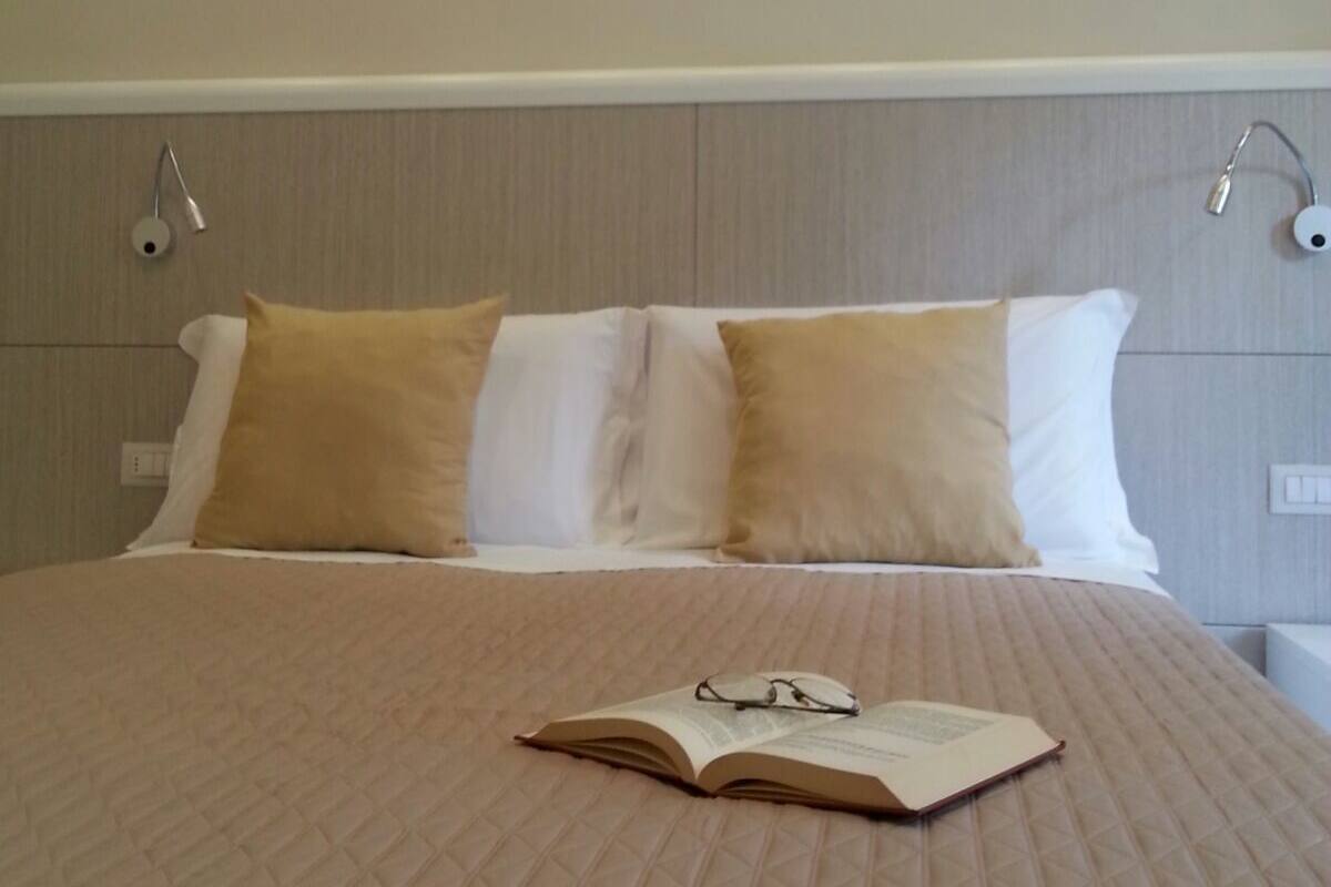 Un lit bien fait, avec une couverture matelassée, deux oreillers et une paire de lunettes posées sur un livre ouvert.