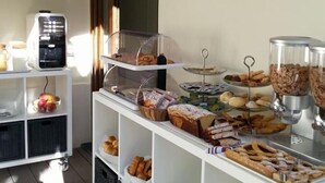 Een buffetopstelling met diverse etenswaren, waaronder gebak, brood en fruit, op een witte wagen met planken.