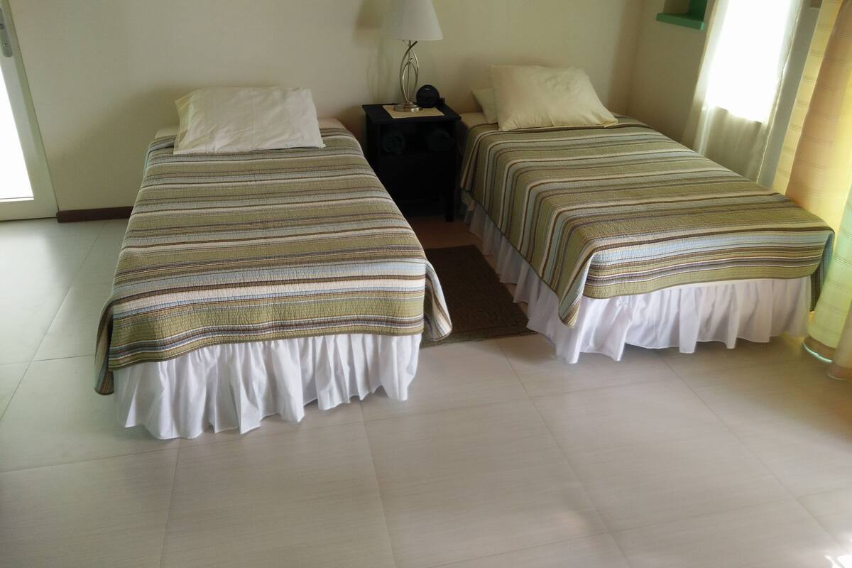 Habitación de hotel con dos camas, una mesita de noche, una lámpara y una ventana con cortinas.
