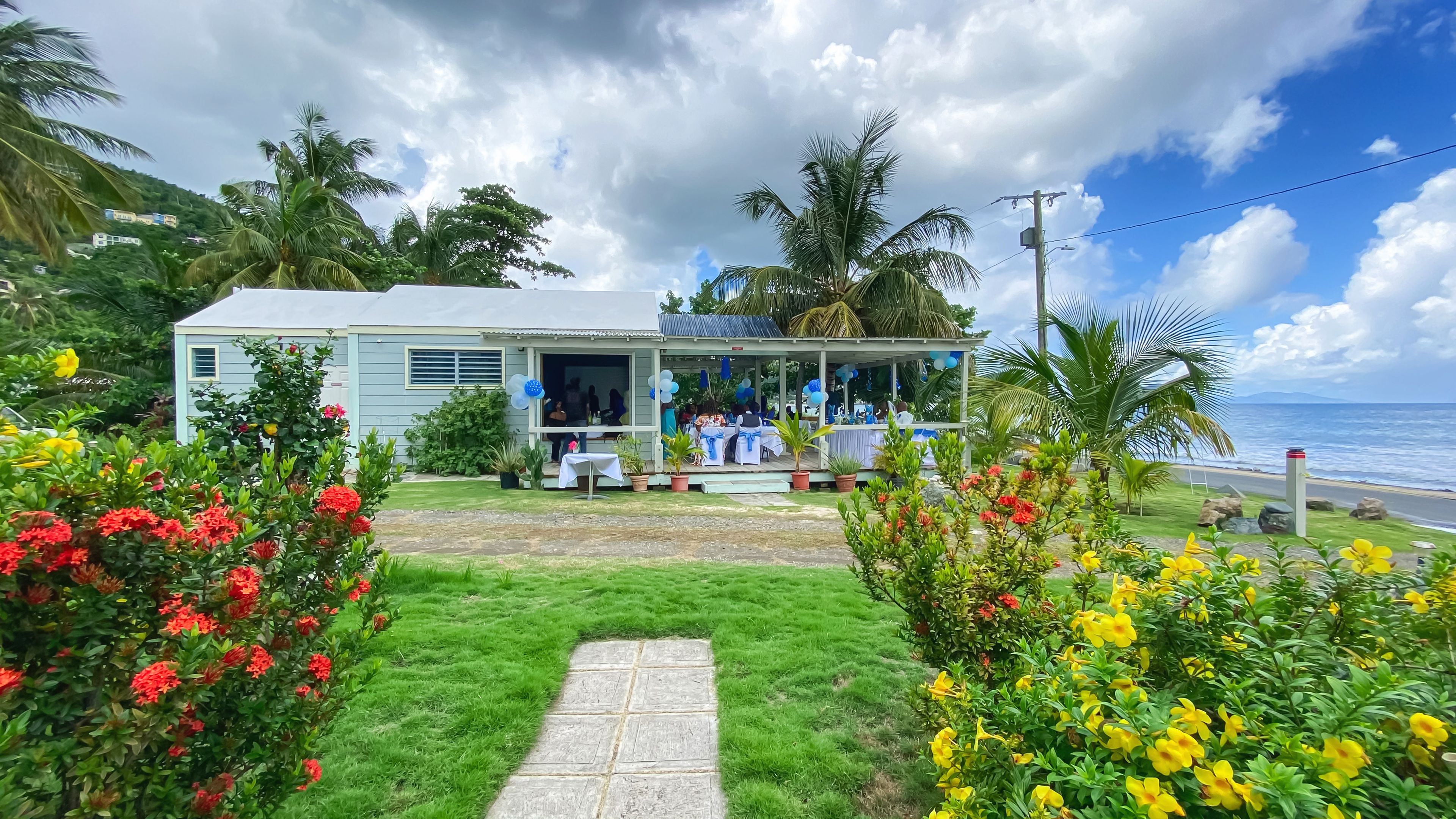 A beachfront property with a covered outdoor area, a grassy lawn, and tropical vegetation.