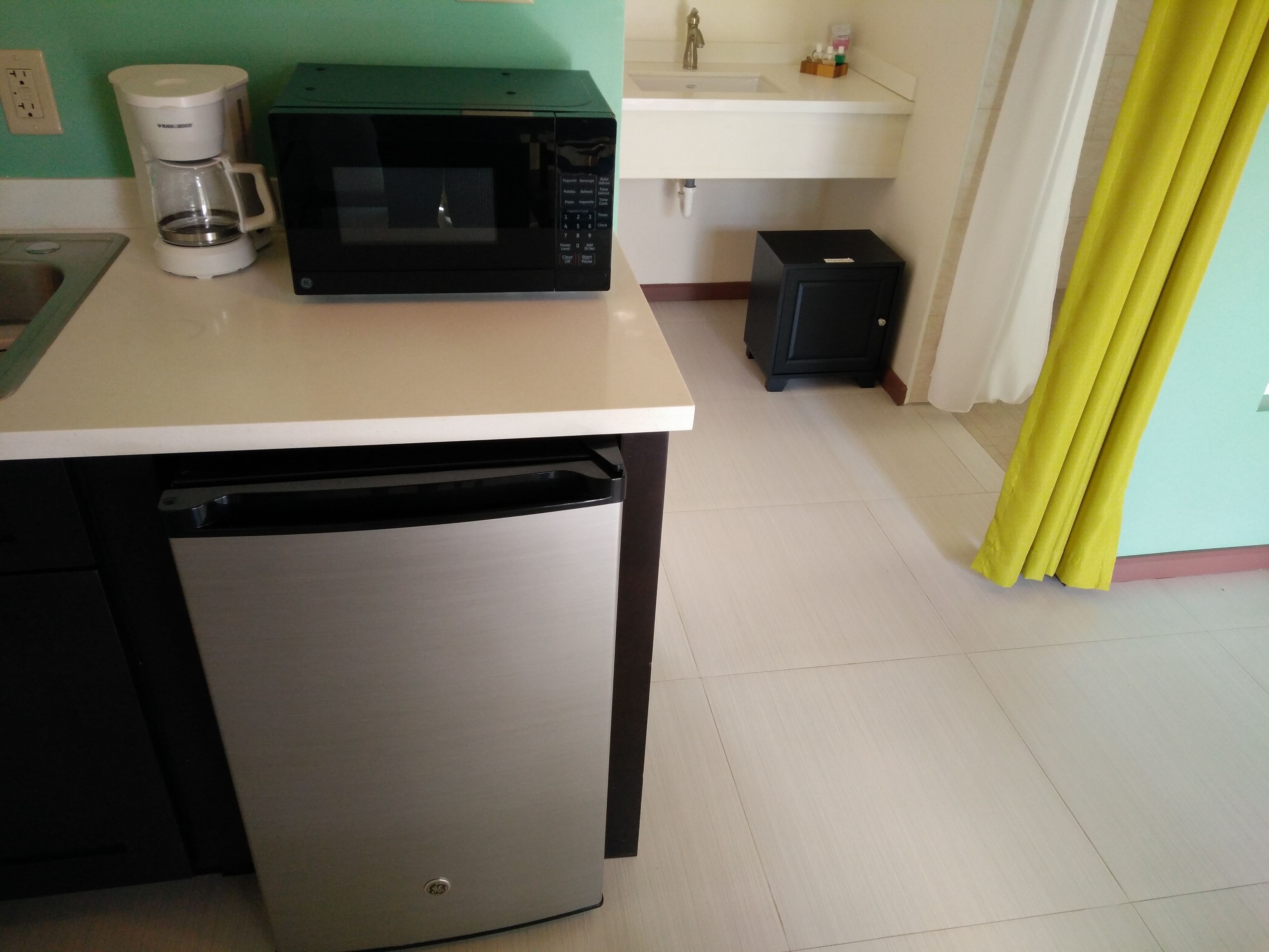 Een kleine keuken met een magnetron, koffiezetapparaat en een kleine koelkast.
