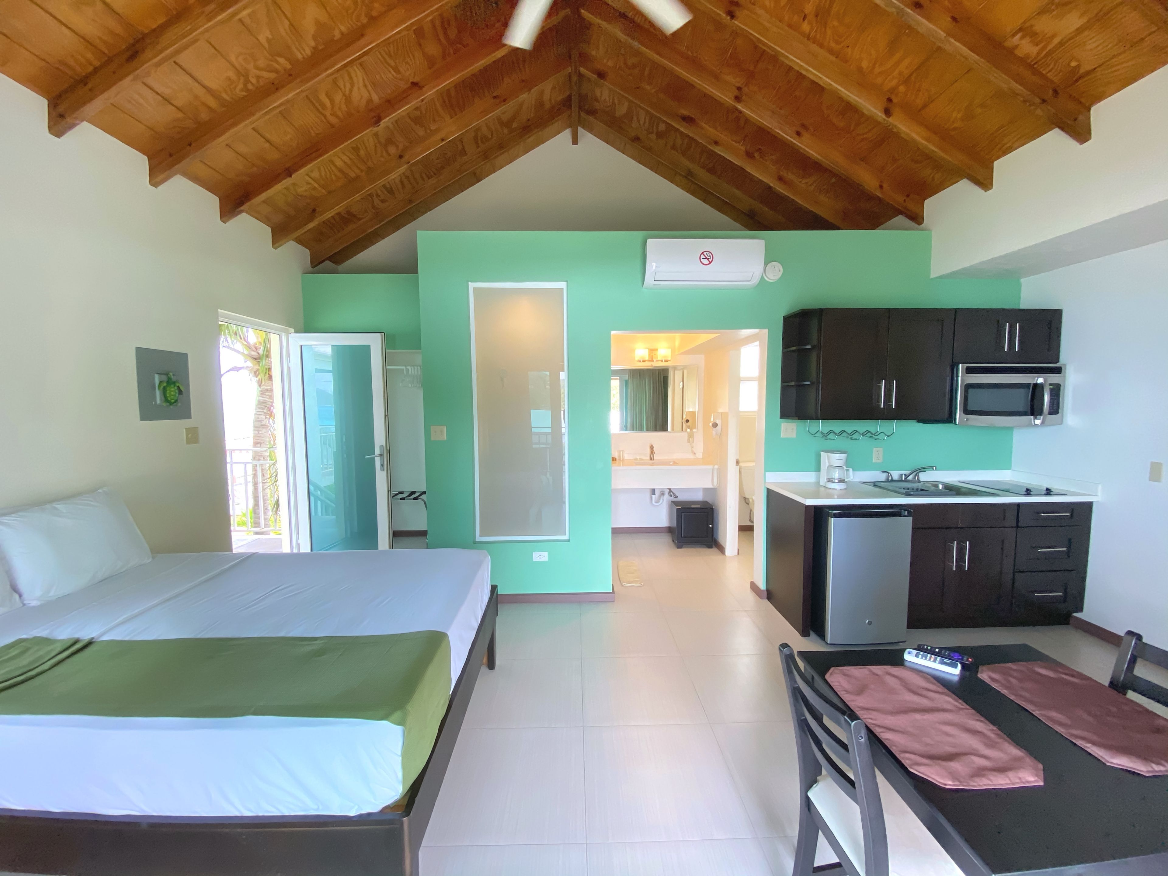 A room with a bed, a kitchenette, and a bathroom visible through an open door.