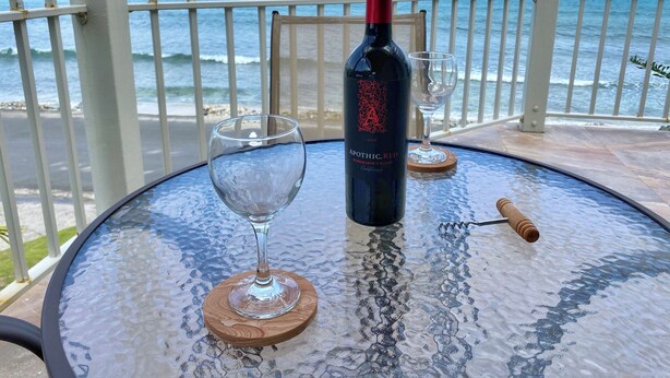 A bottle of Apothic Red wine on a glass table with two wine glasses and a corkscrew, overlooking the ocean. - Ke Villas (West End)