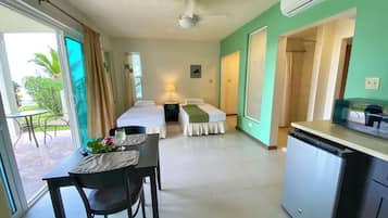 A hotel room with a bed, a desk with a chair, a table with a glass of water, and a kitchenette.
