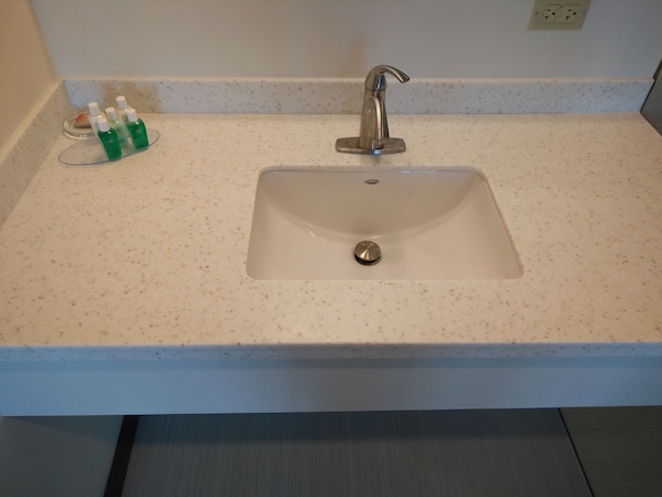 A bathroom sink with a single faucet, a soap dispenser, and a glass soap dish. - Ke Villas (West End)