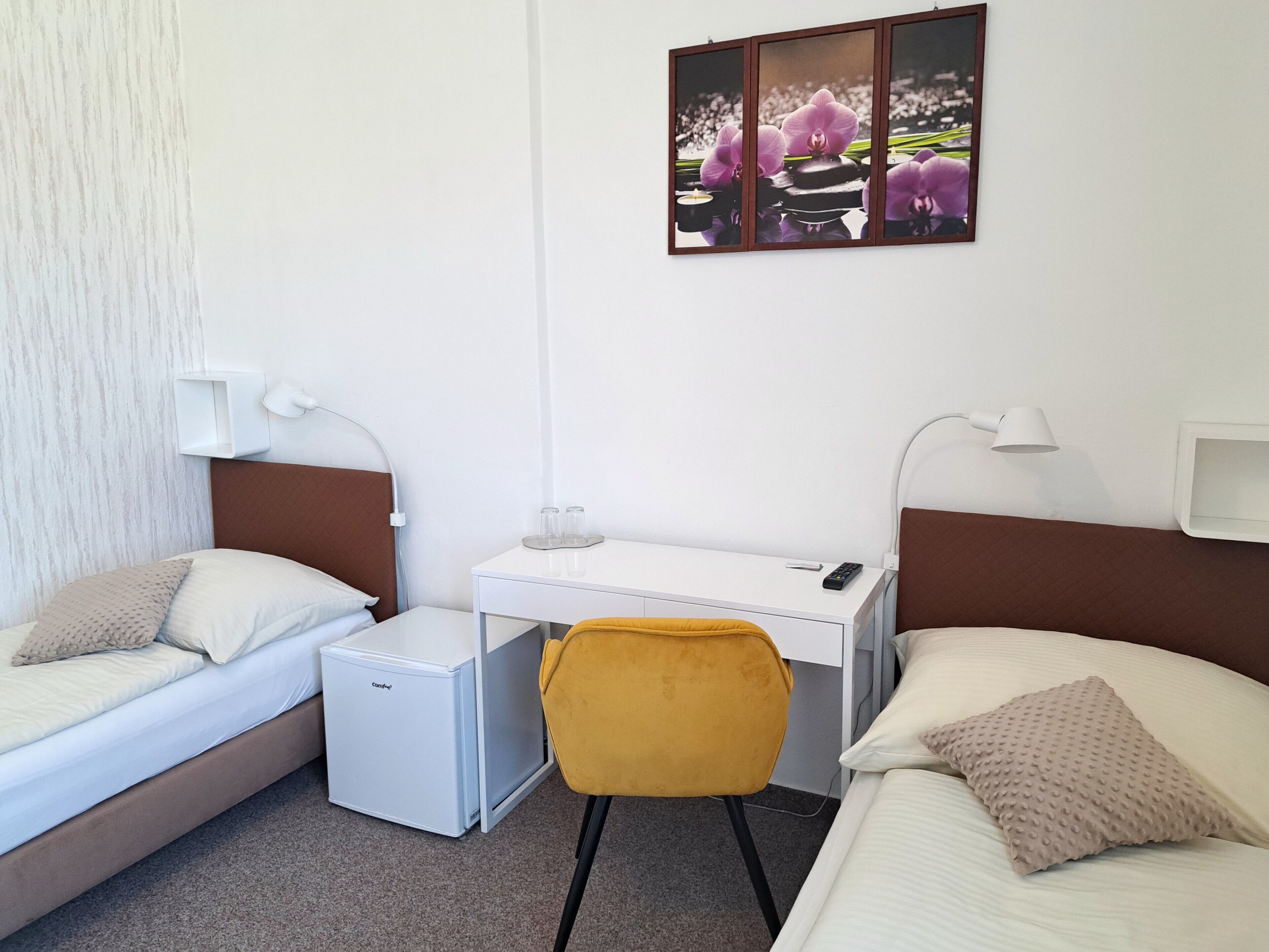 Een hotelkamer met een bed, een bureau met een computer, een stoel en een kleine koelkast.