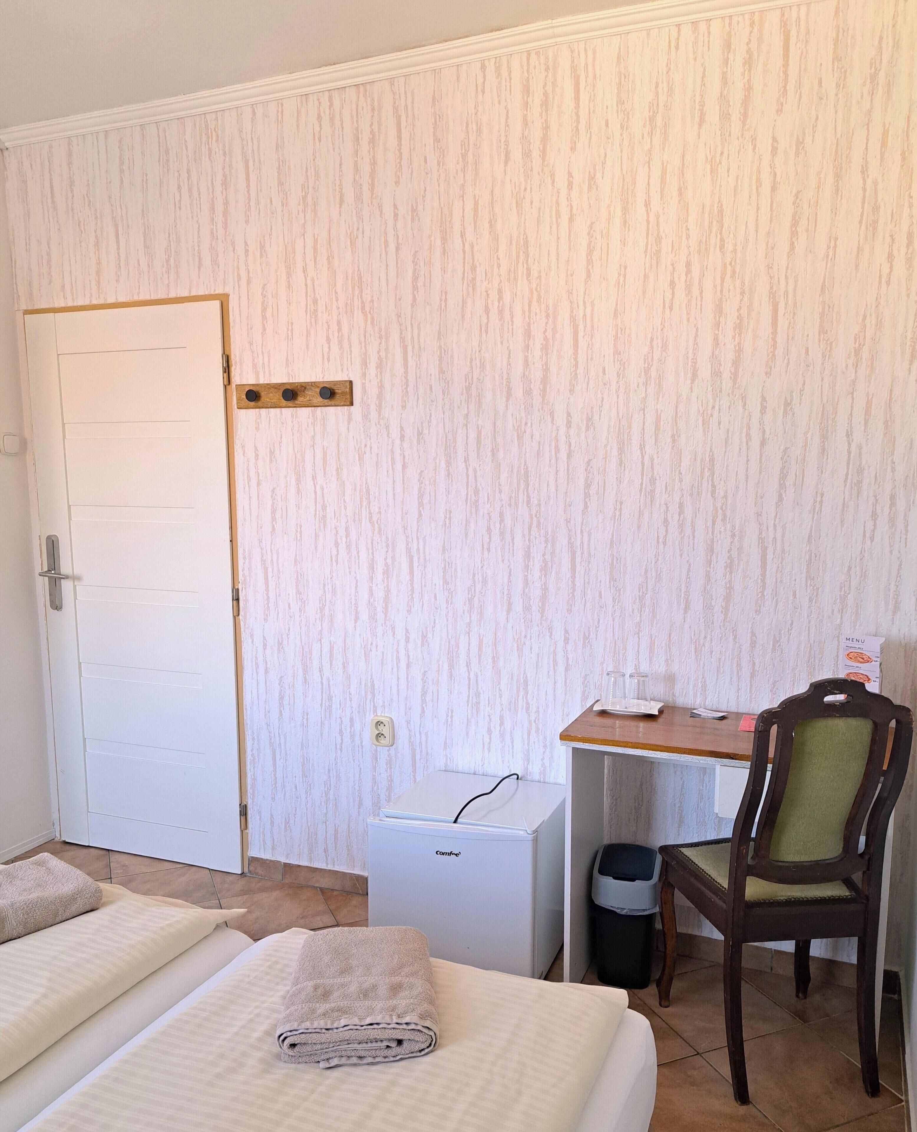 Habitación de hotel con cama, un refrigerador pequeño blanco, un escritorio de madera con una silla y un cesto de basura.