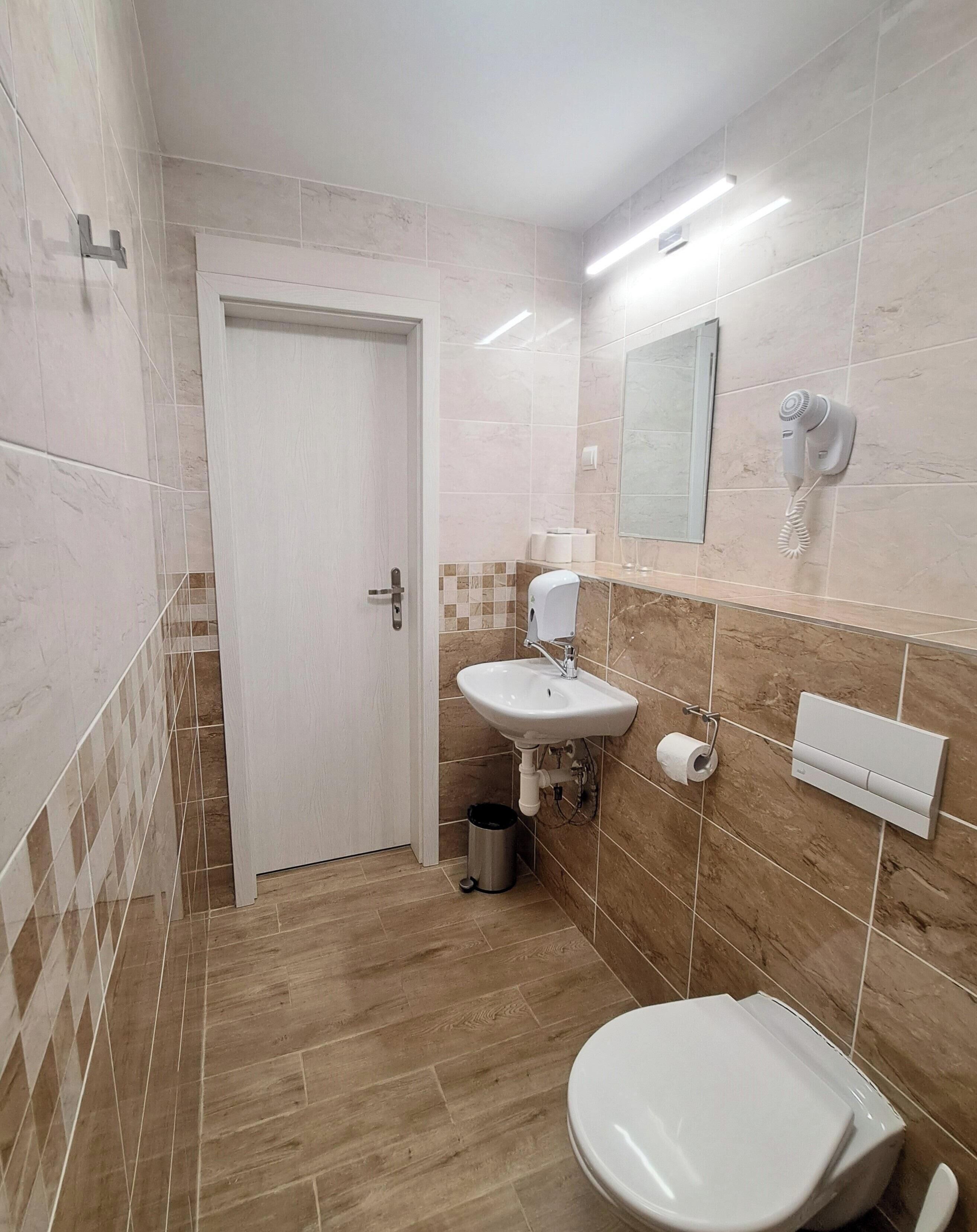 Un baño con inodoro, lavamanos y secador de pelo en la pared.