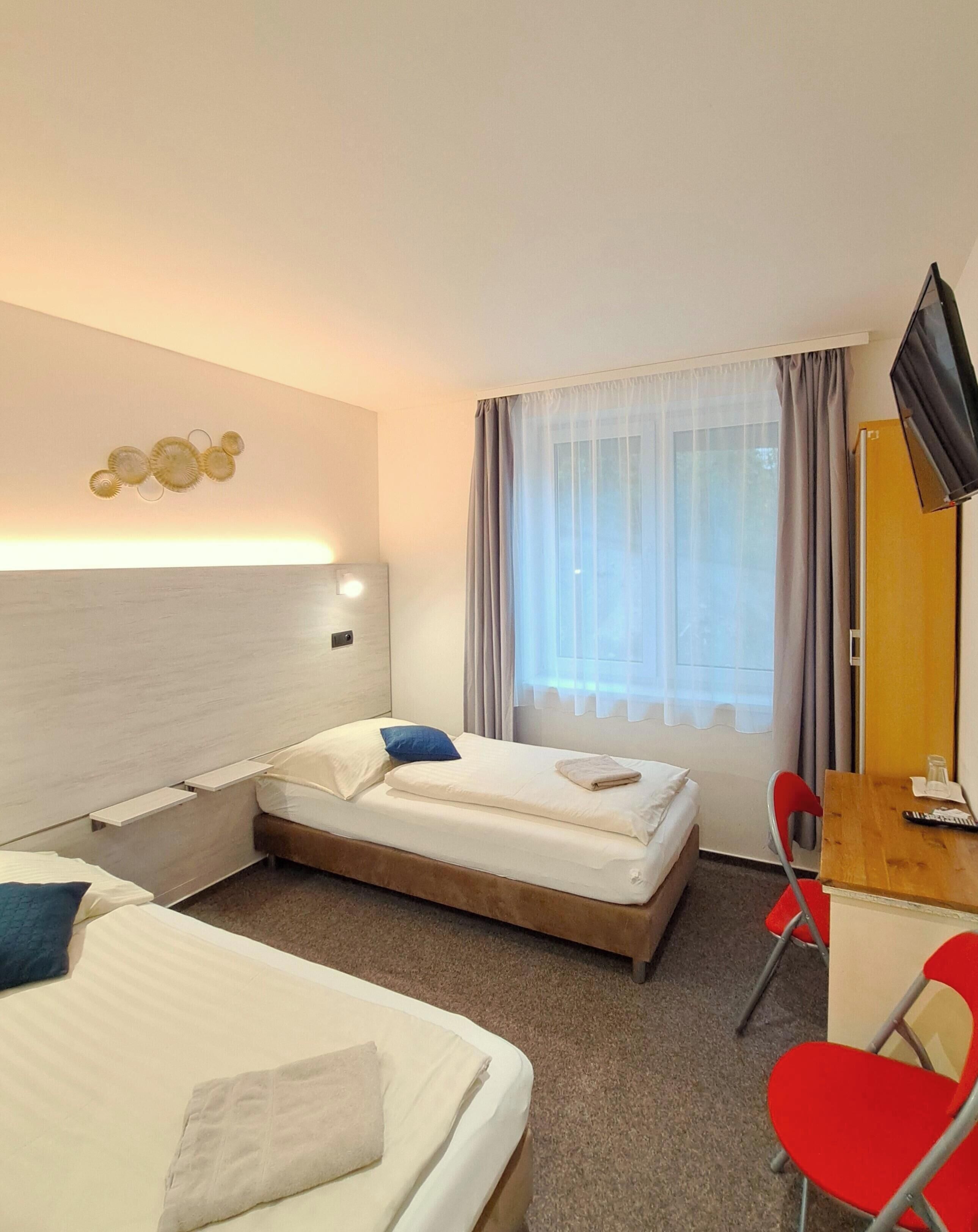 Ein Hotelzimmer mit zwei Betten, einem Schreibtisch, einem Fernseher und einem Fenster mit Vorhängen.