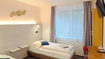 Ein Hotelzimmer mit zwei Betten, einem Schreibtisch, einem Fernseher und einem Fenster mit Vorhängen.