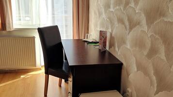 Une pièce avec un plancher en bois, une chaise noire, une petite table avec un menu, un radiateur et une fenêtre avec des rideaux.